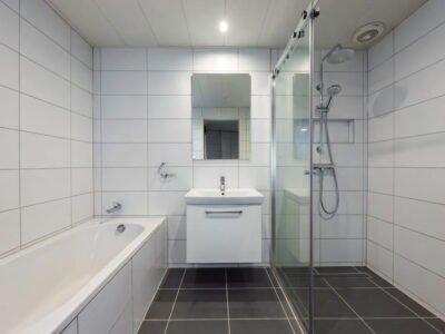 Ruime badkamer met ligbad, glazen inloopdouche, zwevend wastafelmeubel en spiegel met witte wandtegels en donkere vloer — badkamerrenovatie Niscon Group Noord-Brabant