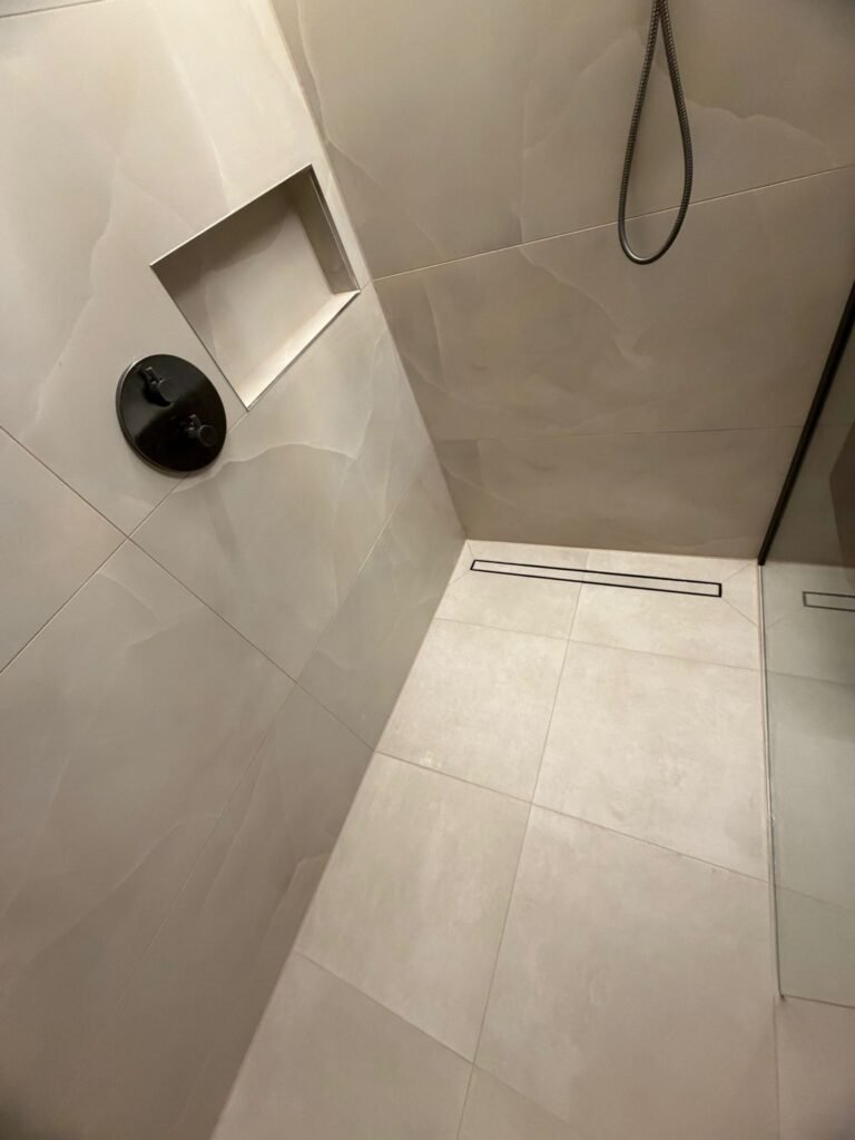 Betegelde douchenis in de wand met handdouche en grootformaat tegels — badkamerrenovatie Niscon Group Noord-Brabant