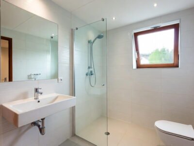 Lichte beige getegelde badkamer met glazen inloopdouche, zwevende wastafel, hangtoilet en grote spiegel — badkamerrenovatie Niscon Group Noord-Brabant