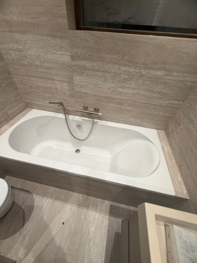 Badkamerwand met travertinlook tegels, inbouwnis en spiegel in een gerenoveerde badkamer — Niscon Group Noord-Brabant
