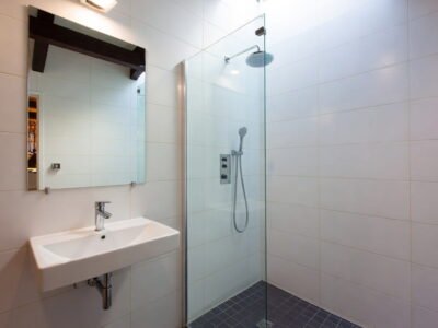 Witte badkamer met glazen inloopdouche, regendouche, zwevende wastafel en spiegelkast met donkere mozaïek douchevloer — badkamerrenovatie Niscon Group Noord-Brabant