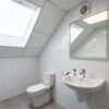 Badkamer met toilet en wastafel onder schuin dak met dakraam, witte wandtegels en grijze vloertegels — badkamerrenovatie Niscon Group Noord-Brabant