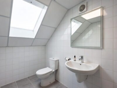Badkamer met toilet en wastafel onder schuin dak met dakraam, witte wandtegels en grijze vloertegels — badkamerrenovatie Niscon Group Noord-Brabant
